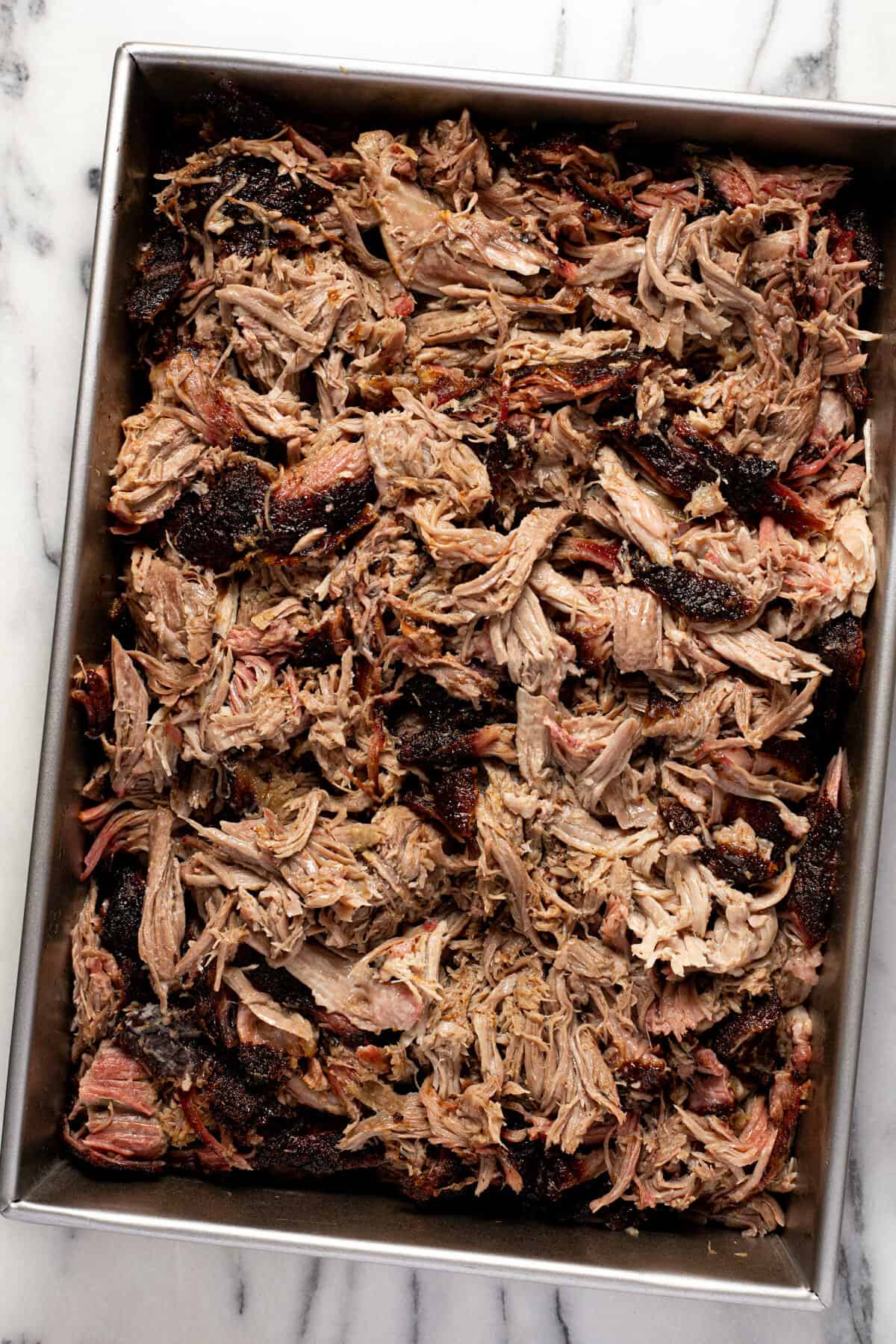 Metal pan filled with shredded smoked pork butt.