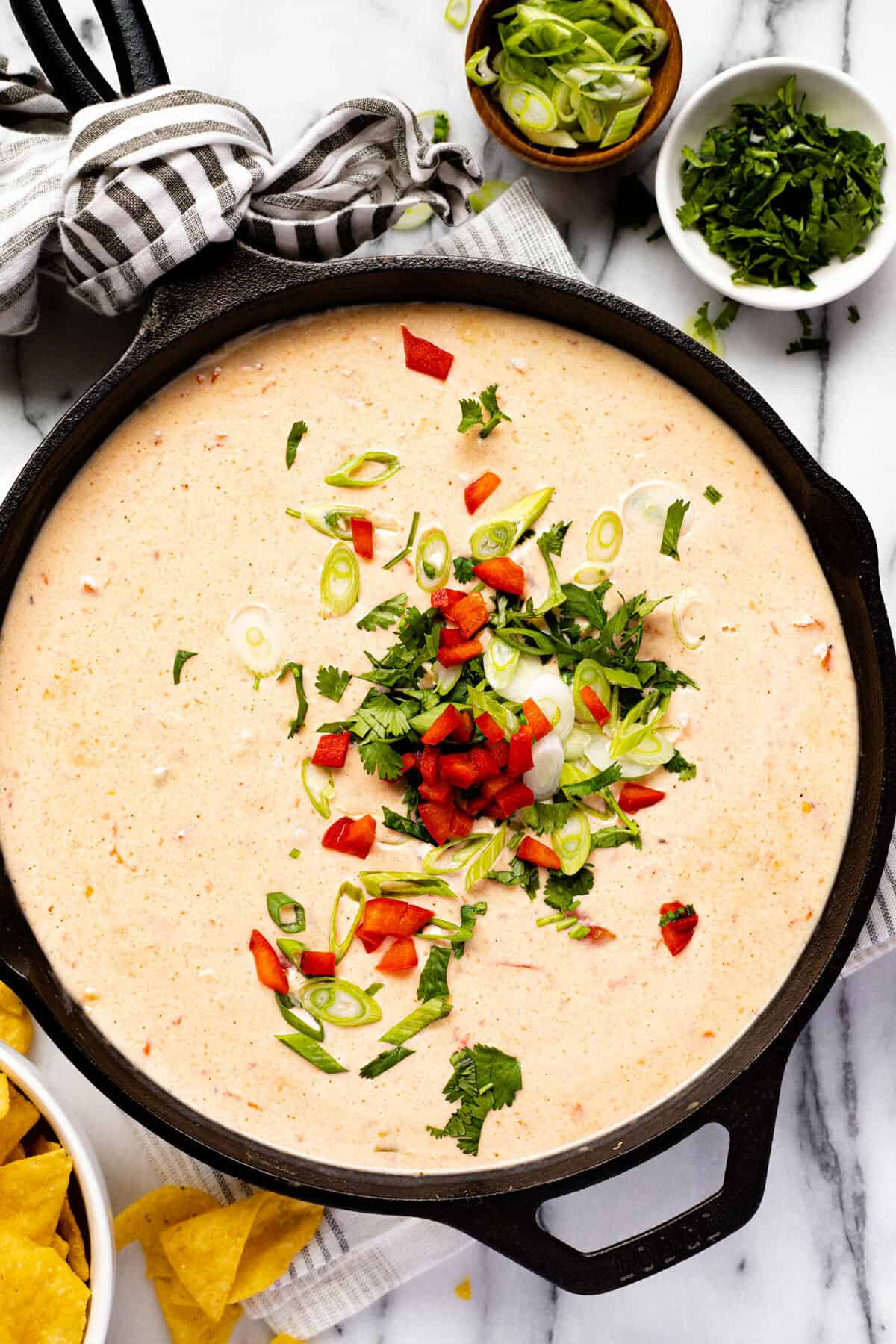 Large cast iron pan filled with homemade smoked queso dip garnished with green onion