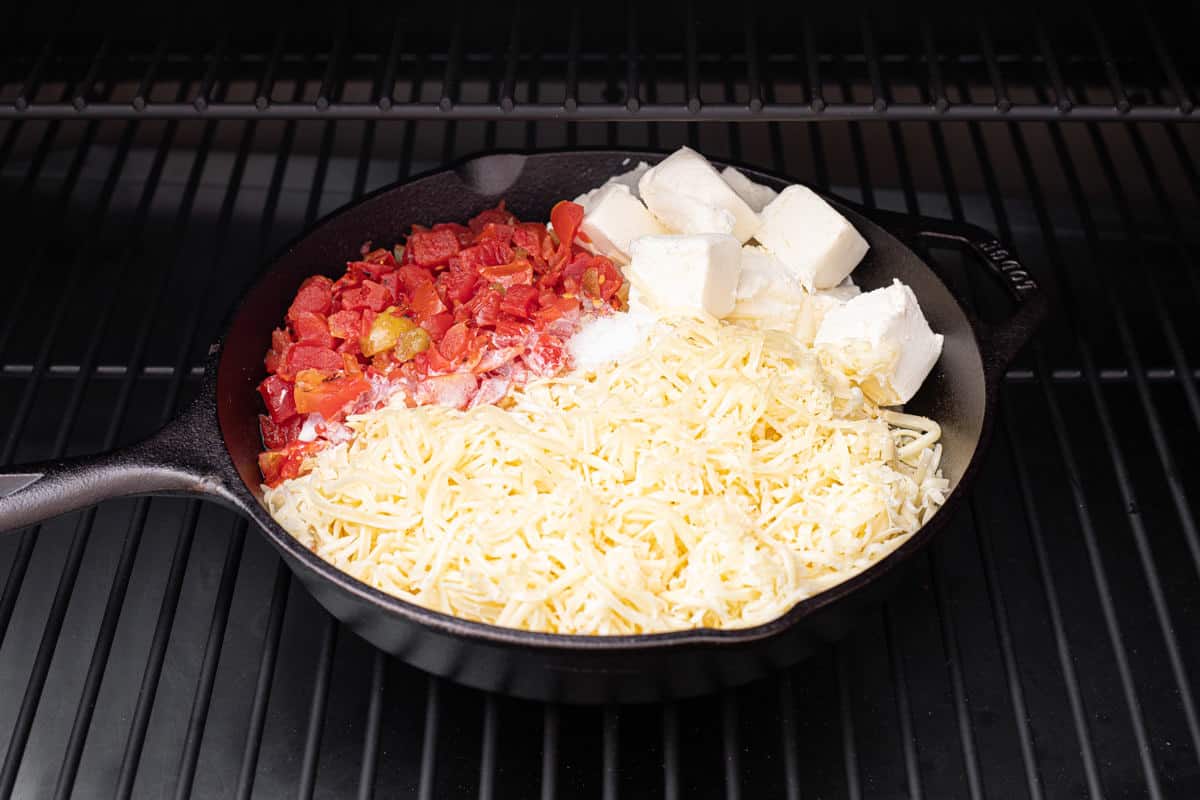Grill with a cast iron skillet with ingredients to make smoked queso