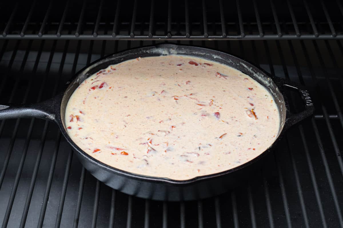 Cast iron skillet with queso dip on a grill.
