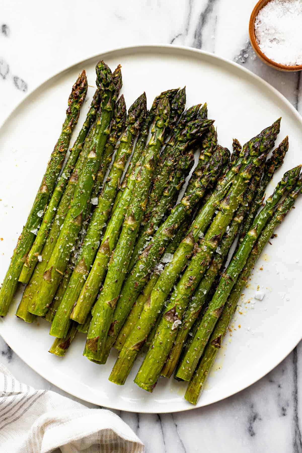 White plate filled with air fried asparagus garnished with finishing salt
