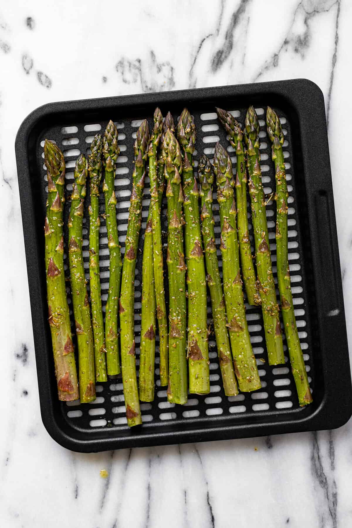 Seasoned asparagus spears on a black air frying tray