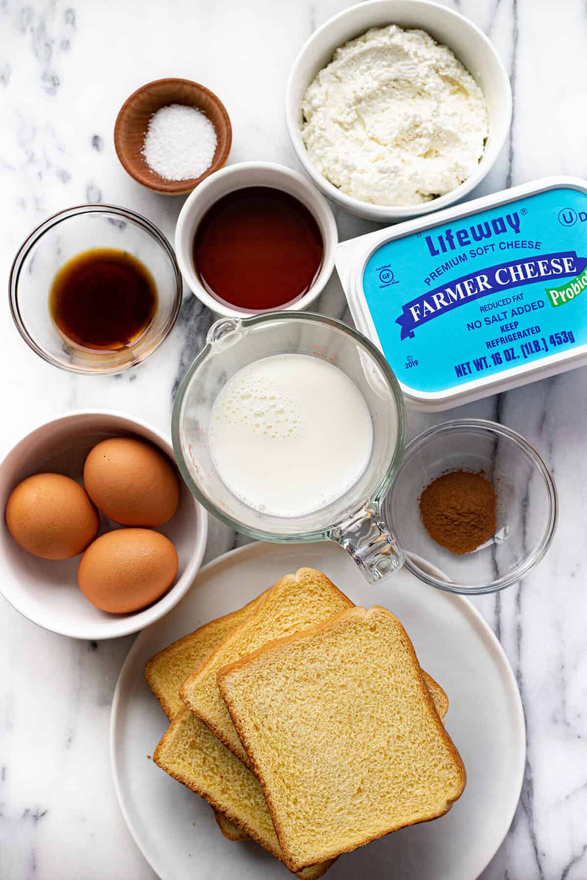 A white marble countertop with bowls of ingredients to make air fryer French toast.