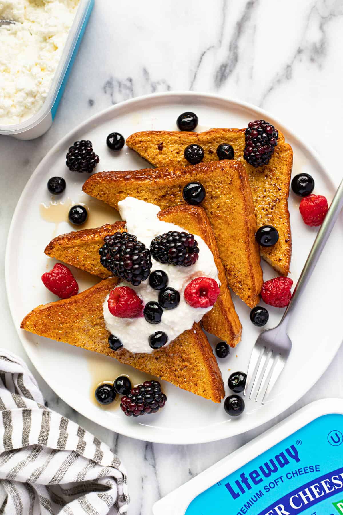4 triangles of French toast on a white plate with berries and cream.