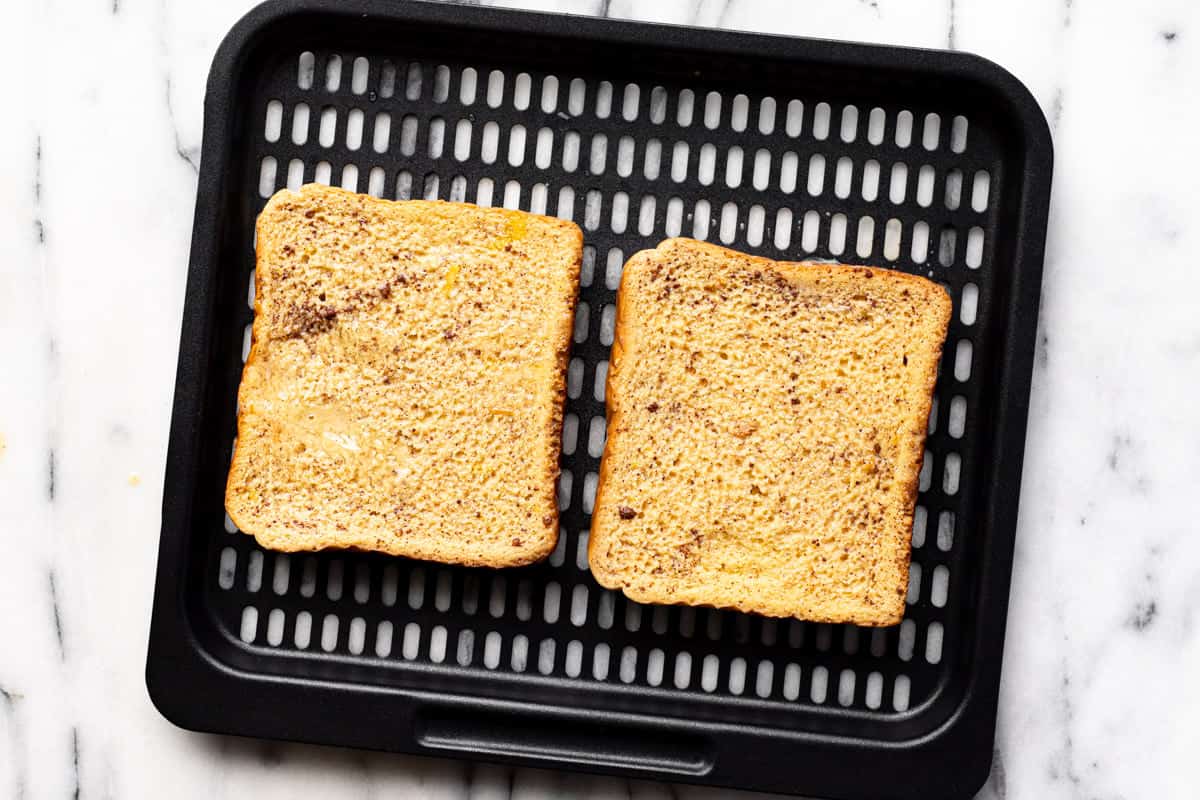 Black air fryer tray with two slices of battered French toast on it.