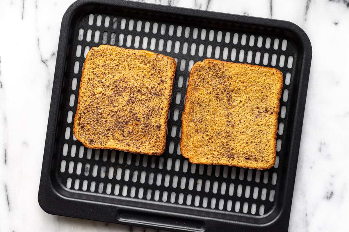 Black air fryer tray with two slices of crispy French toast on it.