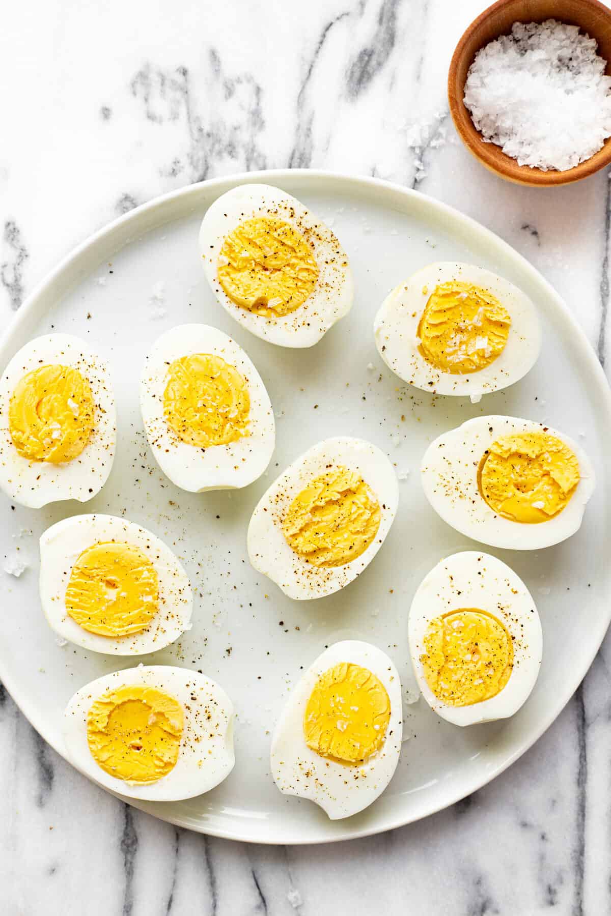 White plate with sliced hard boiled eggs garnished with salt and pepper.