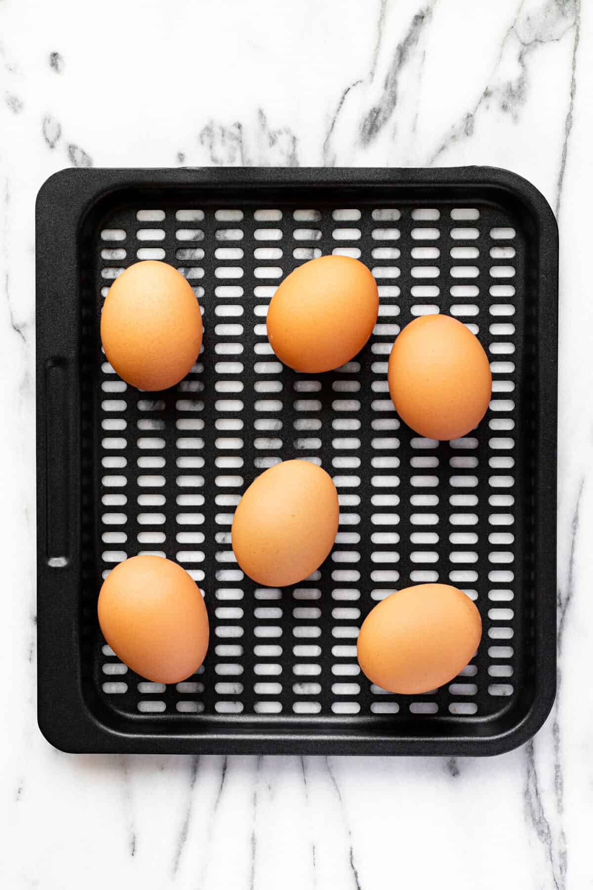 Black air fryer tray with brown eggs on it.