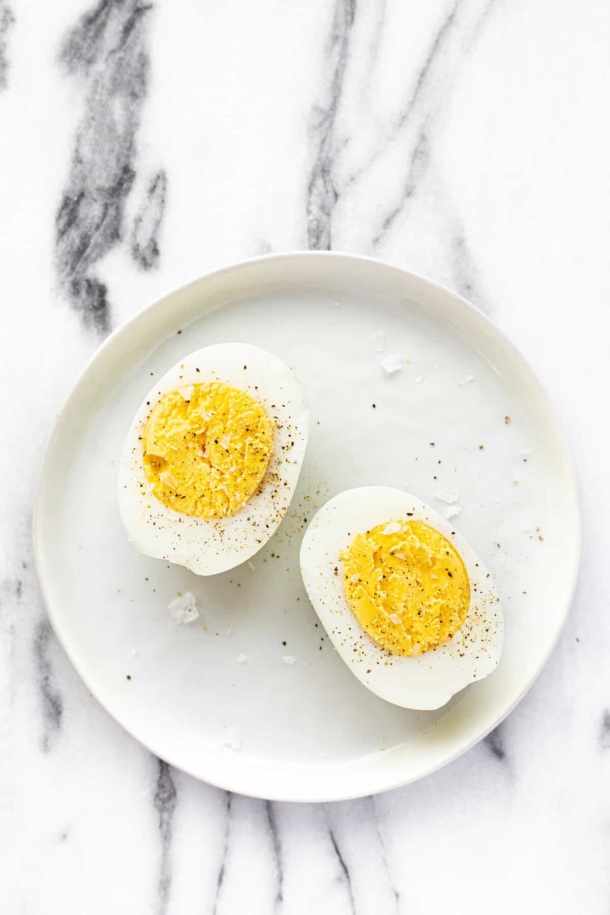 White plate with sliced hard boiled eggs garnished with salt and pepper.