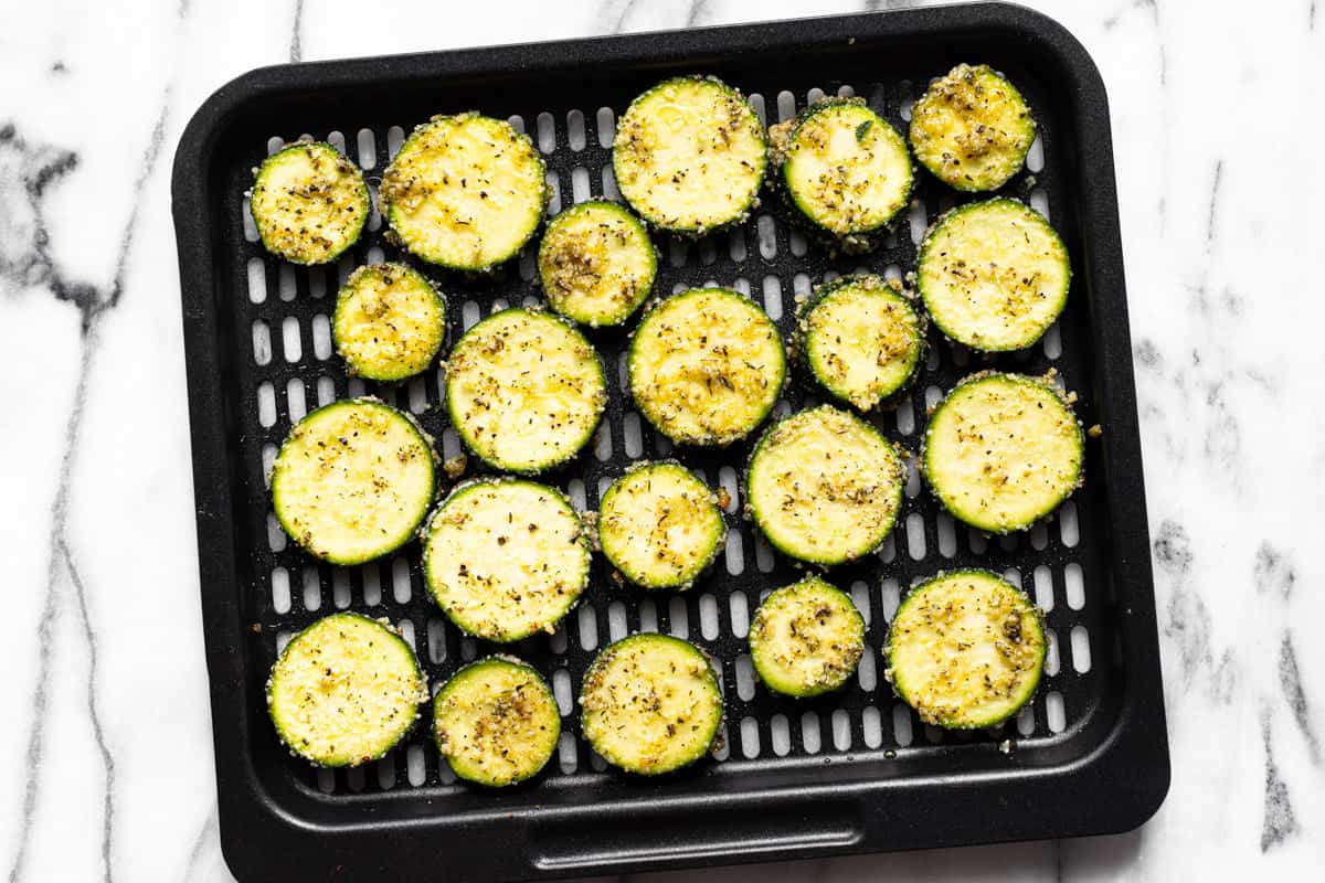 Seasoned slices of zucchini on an air fryer tray.