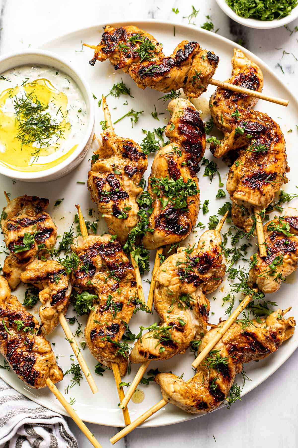 White plate filled with Greek chicken kebabs garnished with parsley and dill.