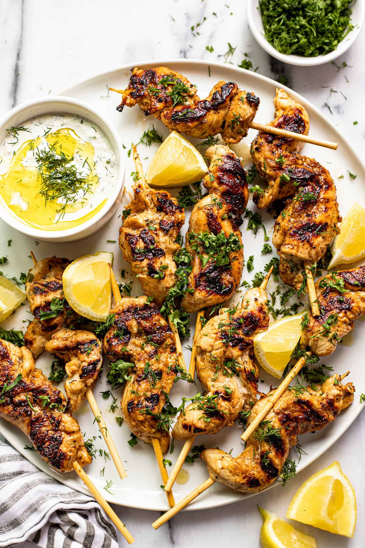 White plate filled with Greek chicken kebabs garnished with parsley and lemon wedges.