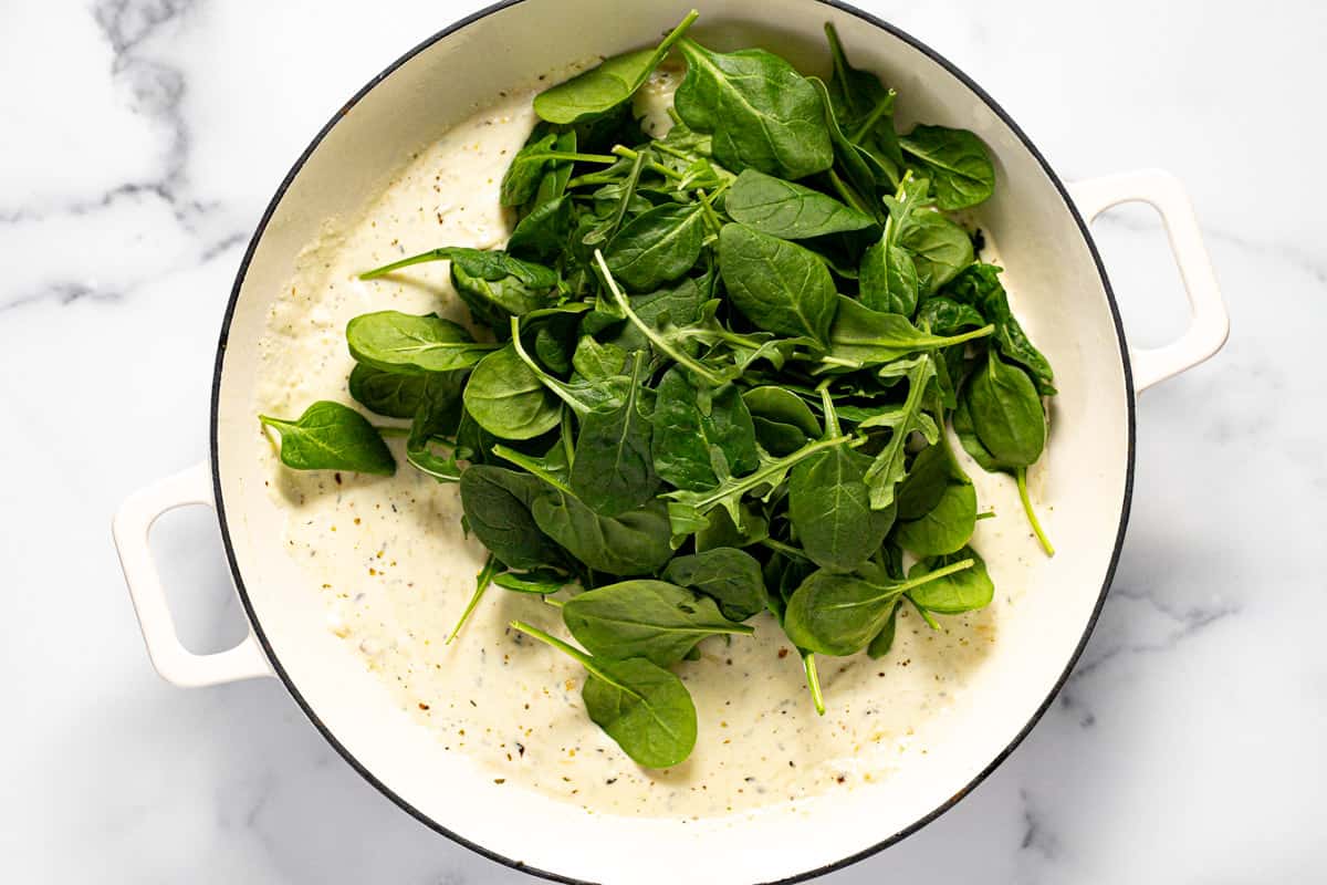 Large white pan filled with creamy ricotta sauce and fresh baby spinach.