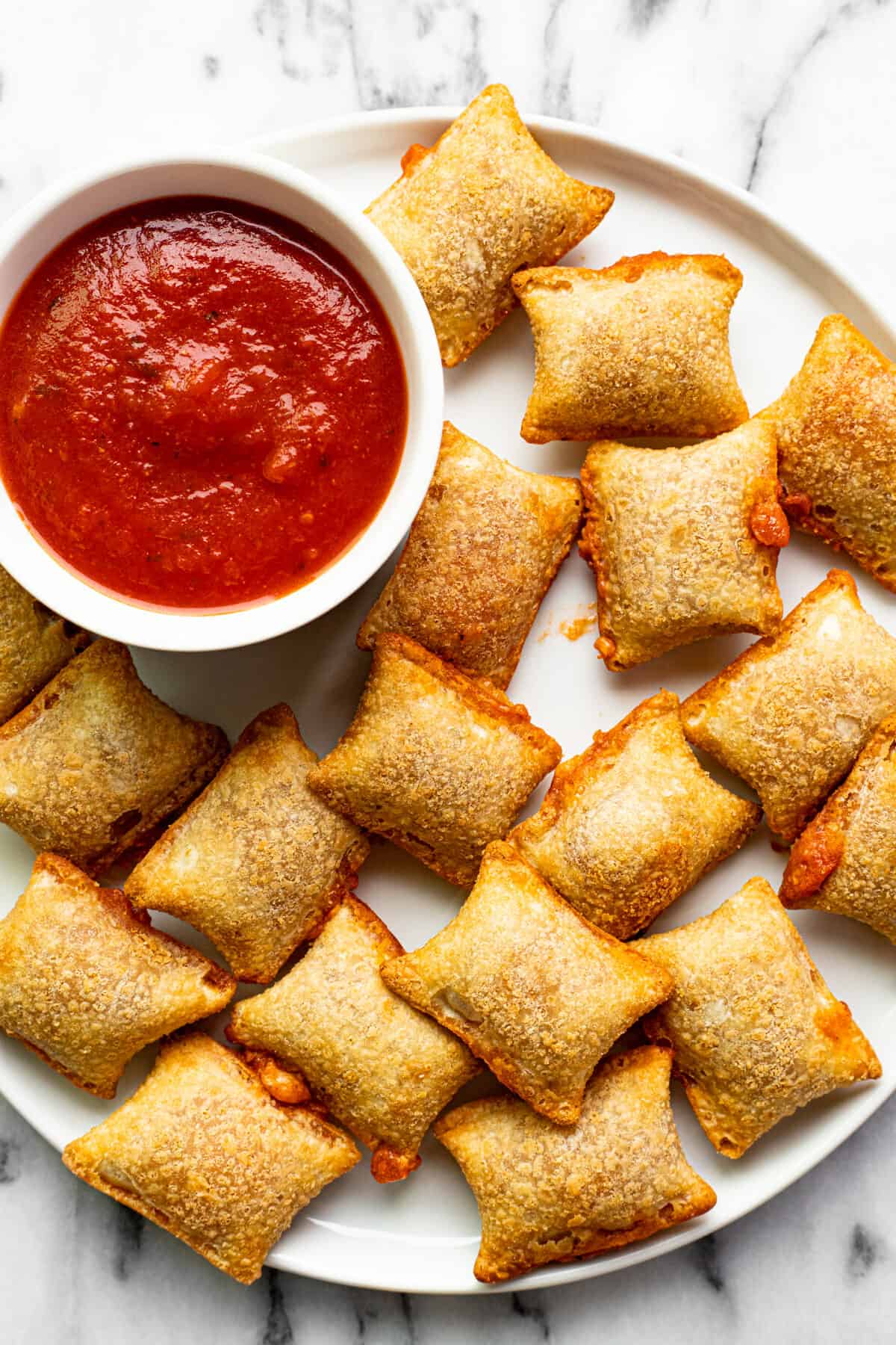 White plate with crispy pizza rolls and a bowl of pizza sauce