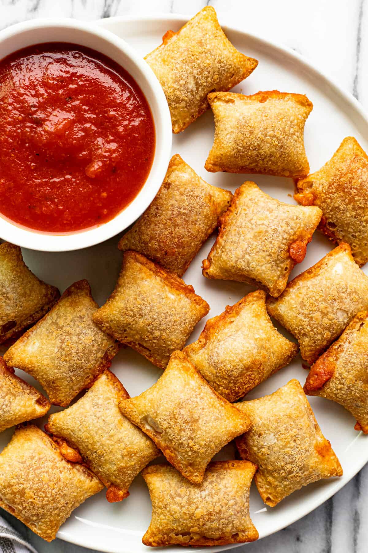 White plate with crispy pizza rolls and a bowl of pizza sauce