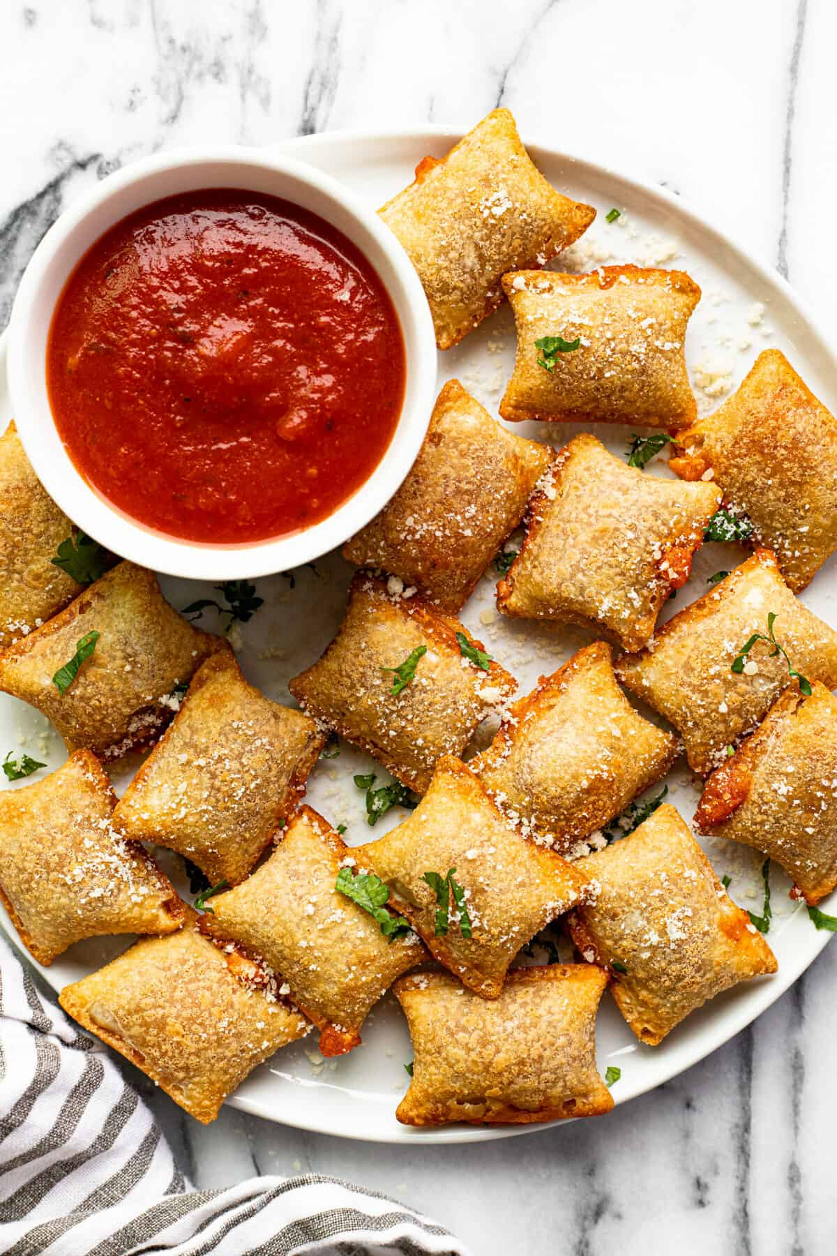 White plate with crispy pizza rolls garnished with Parmesan cheese next to a bowl of pizza sauce