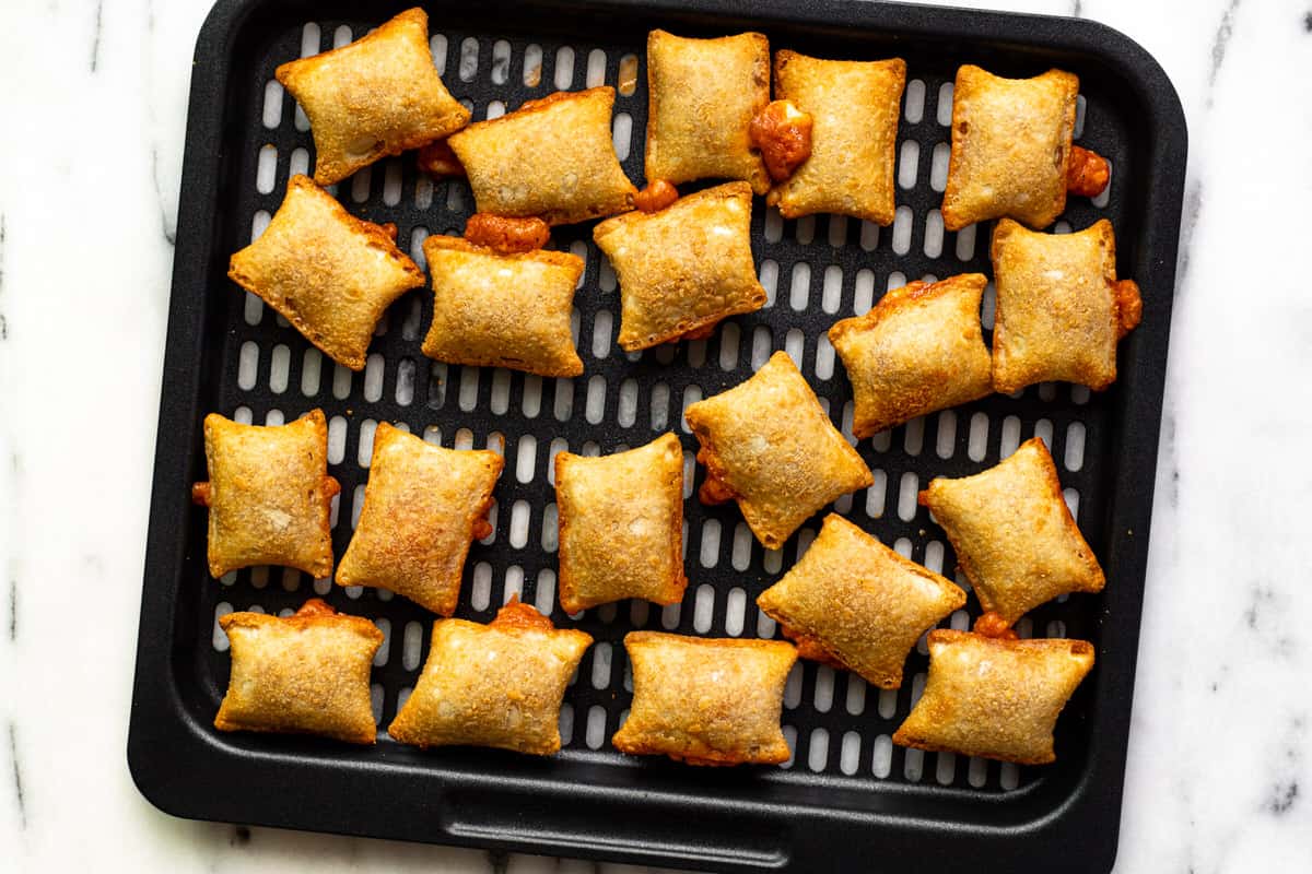 Black air fryer tray with freshly baked pizza rolls on it