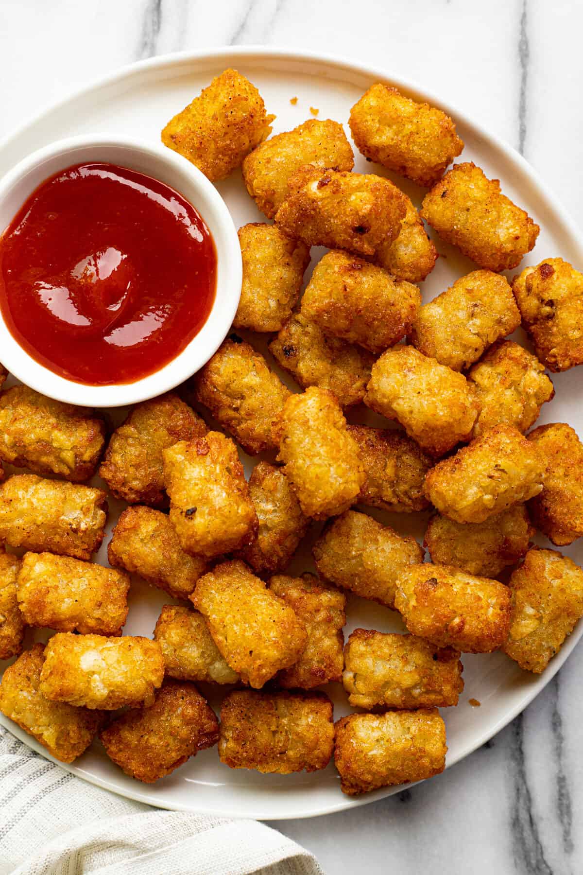 White plate filled with crispy tater tots and a small dish of ketchup.