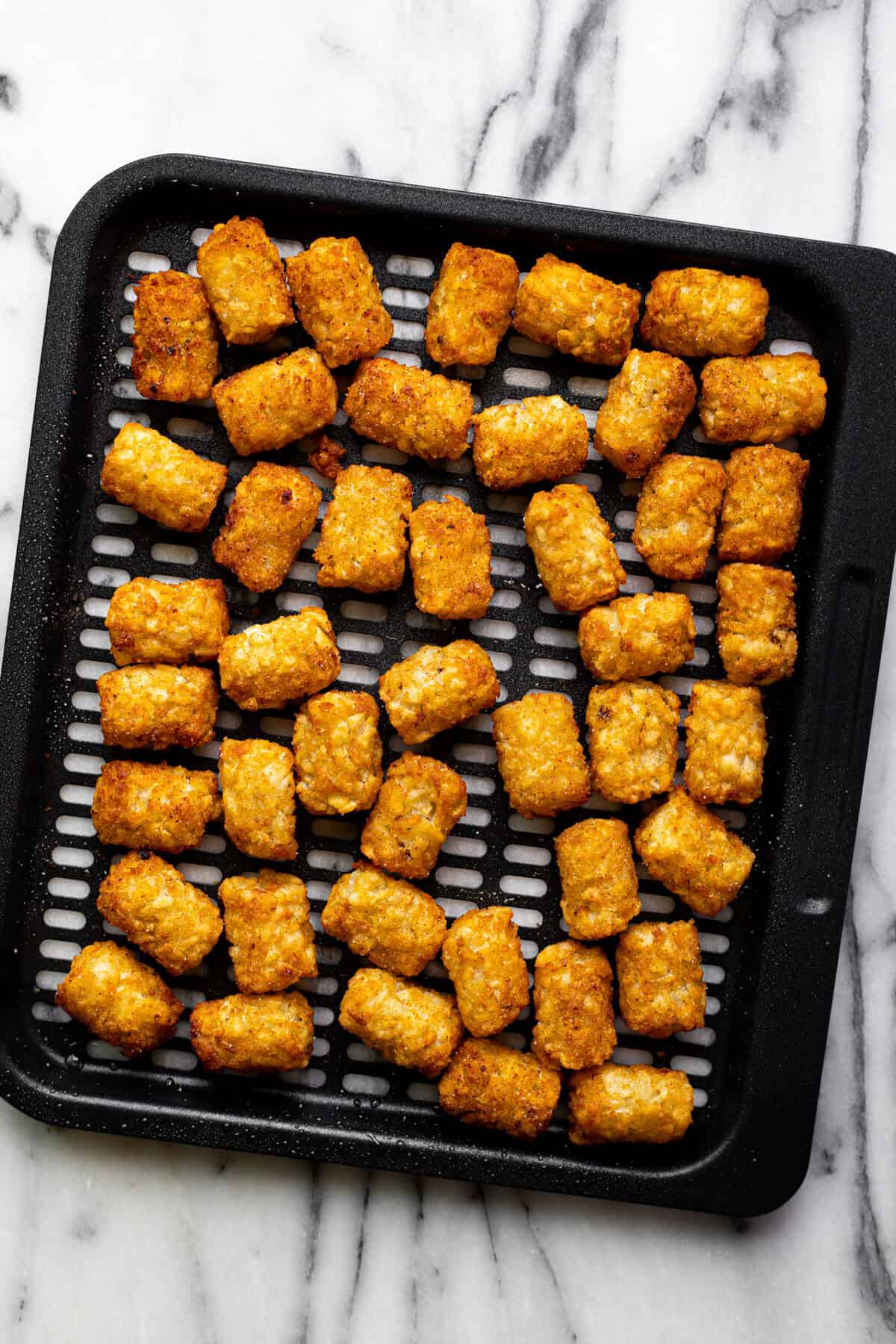 Black air fryer tray with crispy tater tots on it.