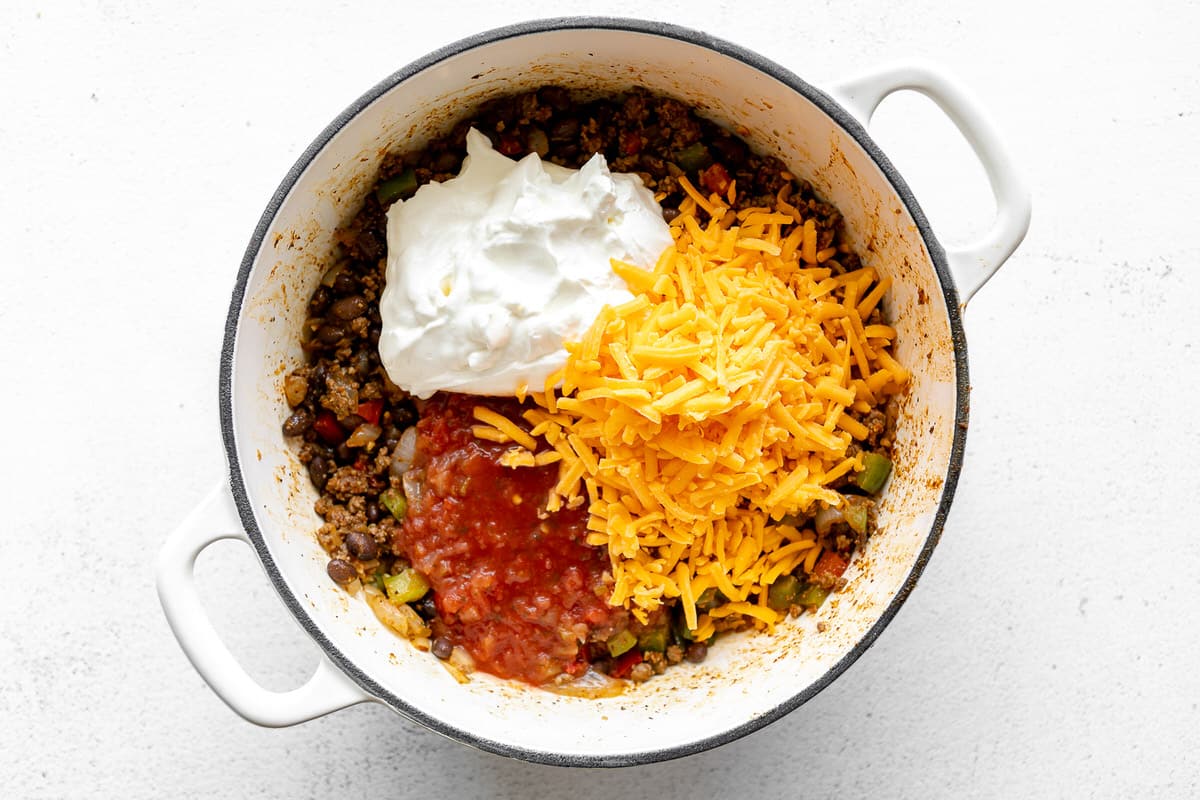 Taco meat, beans, sour cream, salsa, and cheese in a large white pan.