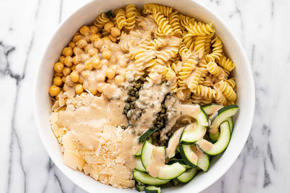 White bowl filled with ingredients to make Caesar kale pasta salad.