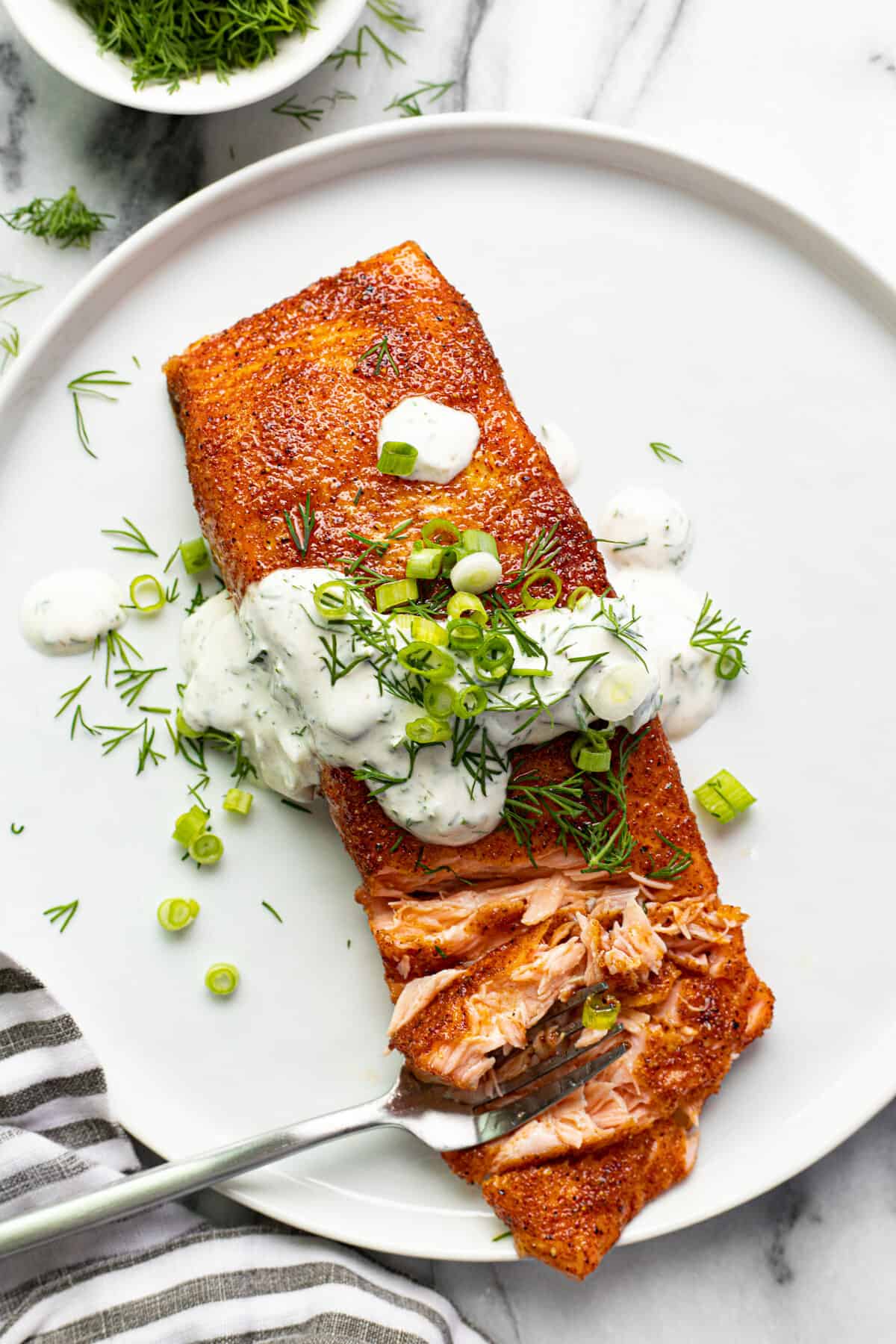 Smoked salmon on a white plate garnished with dill sauce and sliced green onions.