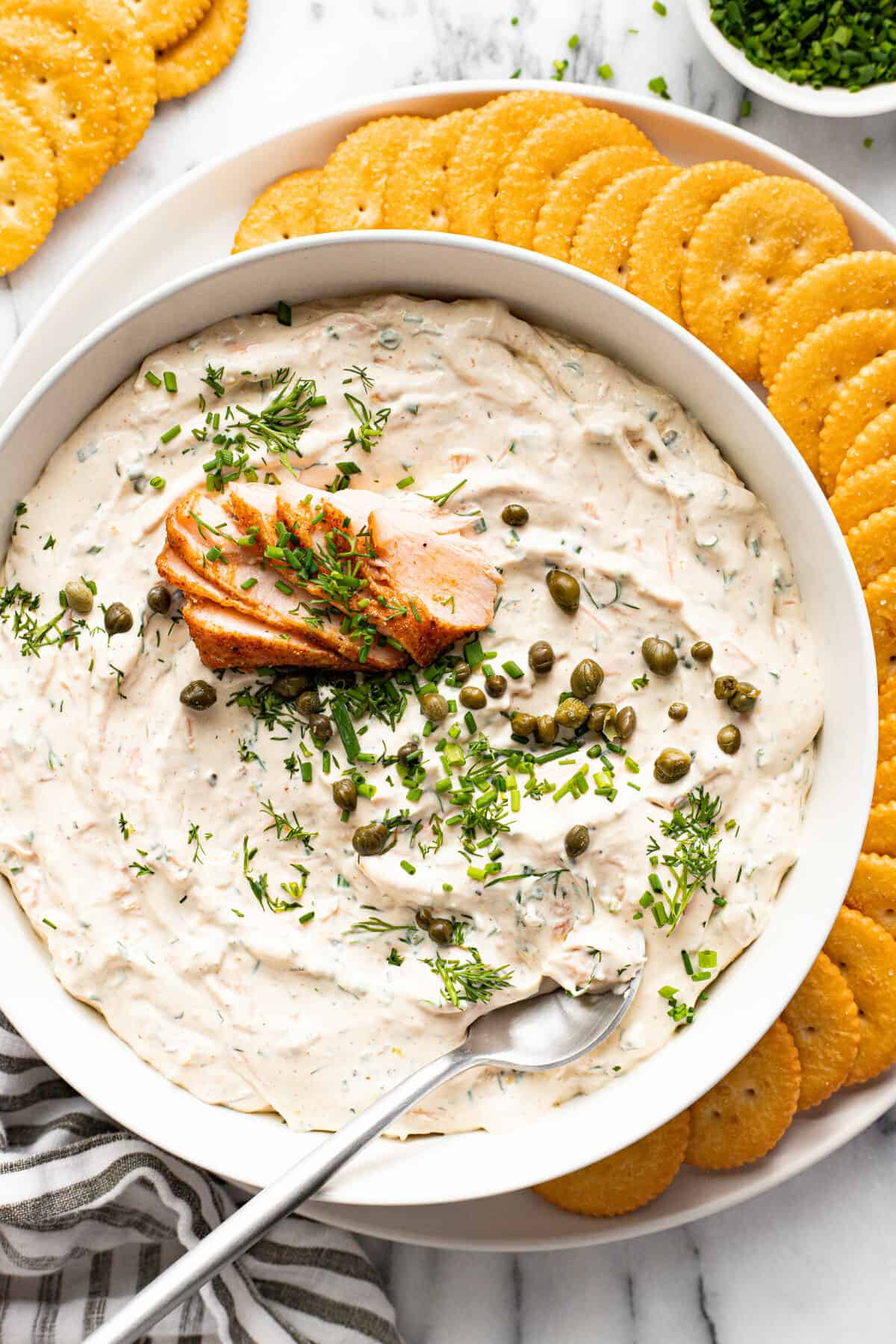 White bowl filled with smoked salmon dip on a white plate with crackers.
