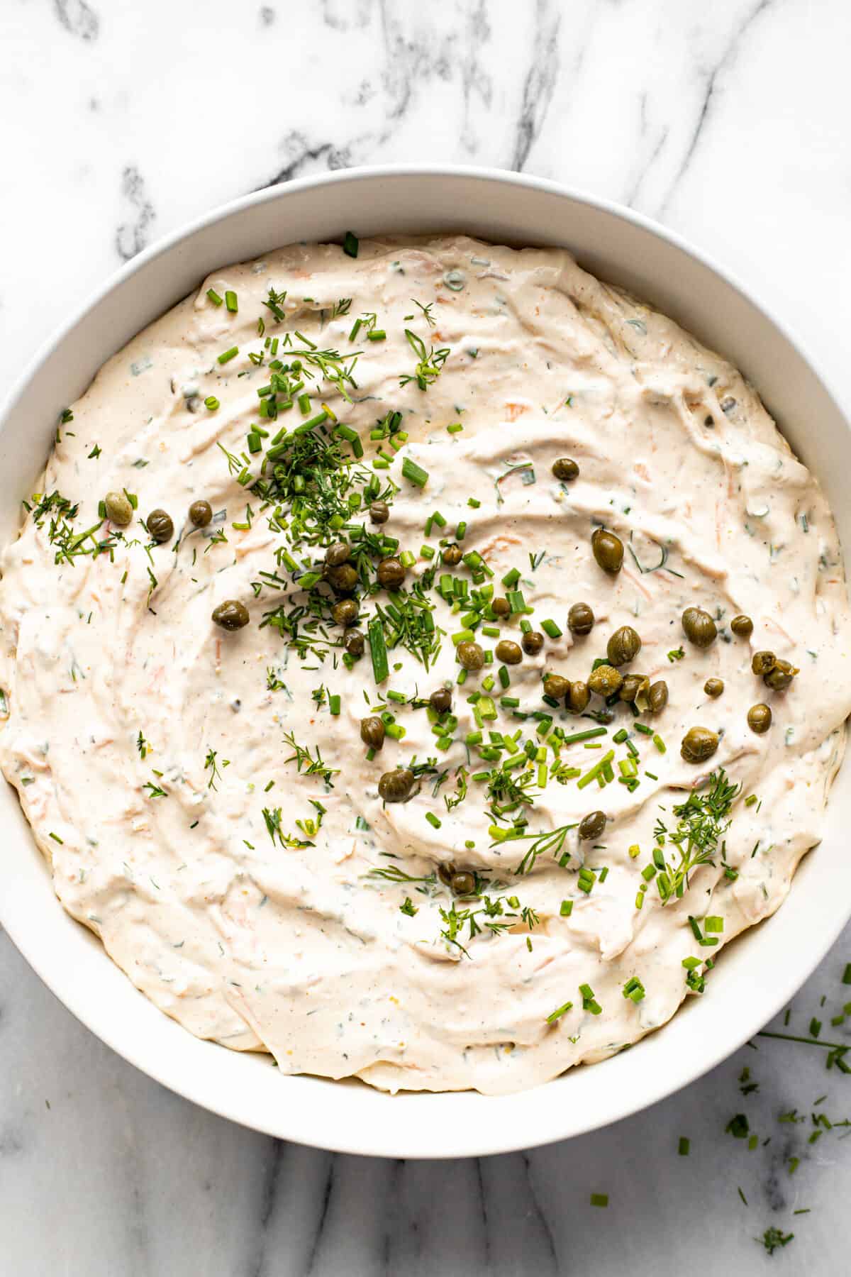 White bowl filled with smoked salmon dip garnished with capers, chives, and dill.