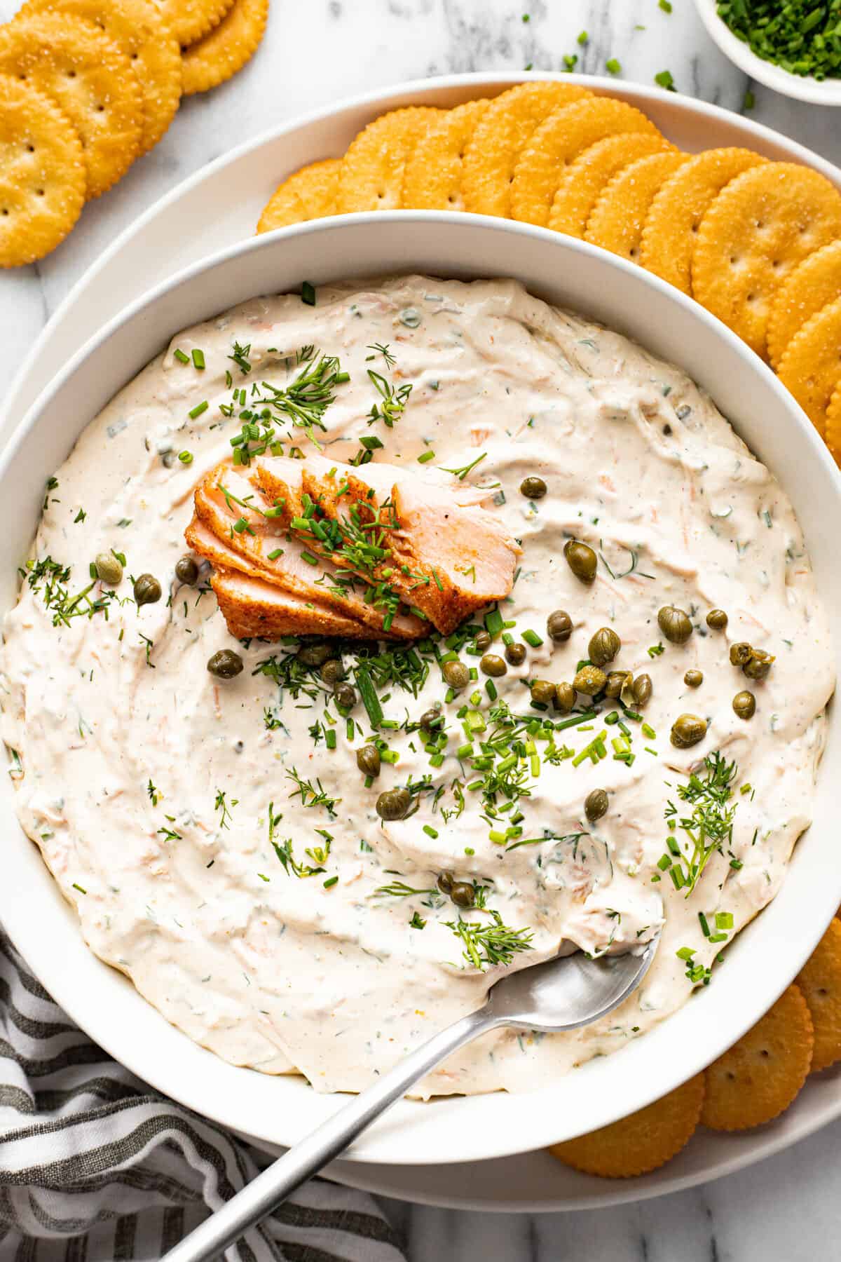 White bowl filled with smoked salmon dip on a white plate with crackers.