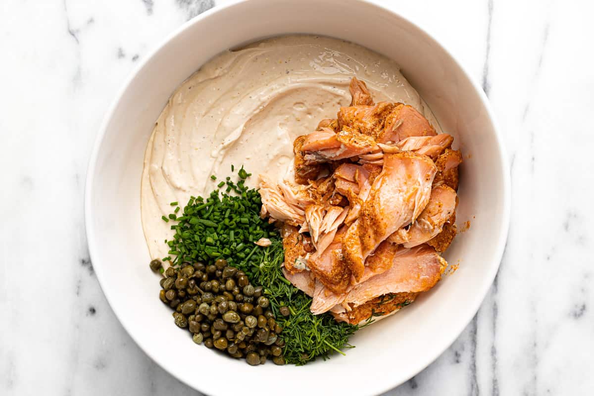 White bowl filled with cream cheese mixture, smoked salmon, capers, and dill.