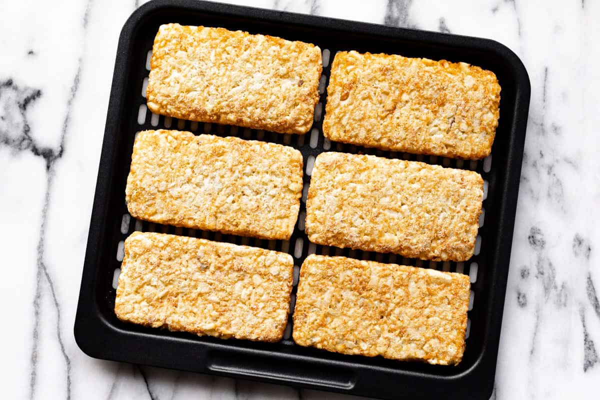 Frozen hash browns on a black air fryer tray.