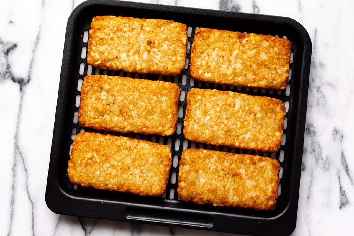 Cooked hash brown patties on a black air fryer tray.