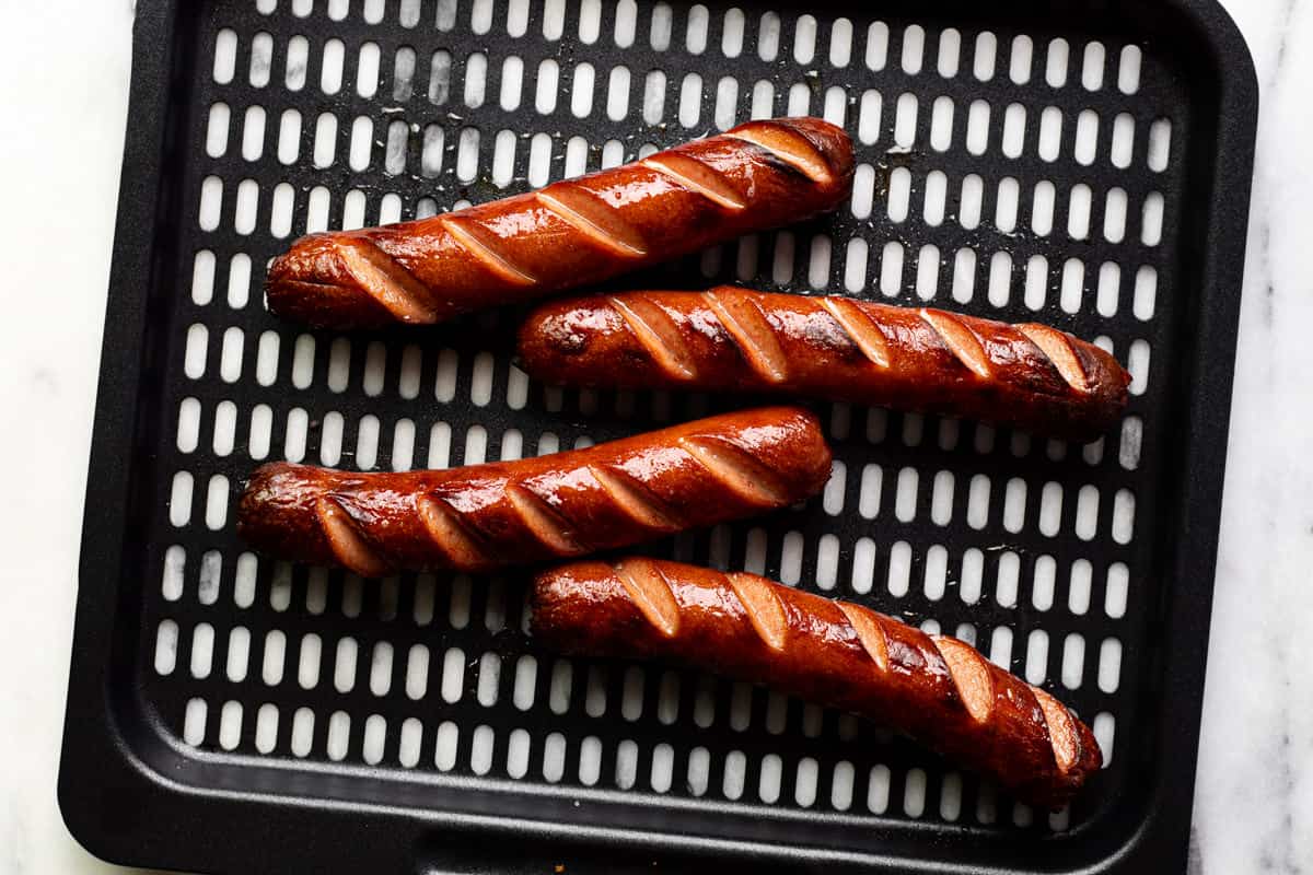 4 cooked hot dogs on an air fryer tray.