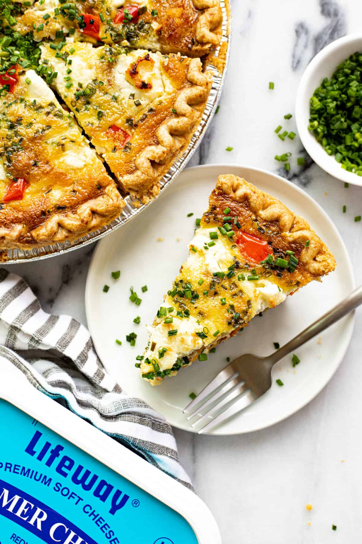 A slice of quiche on a small plate next to the pan of quiche.