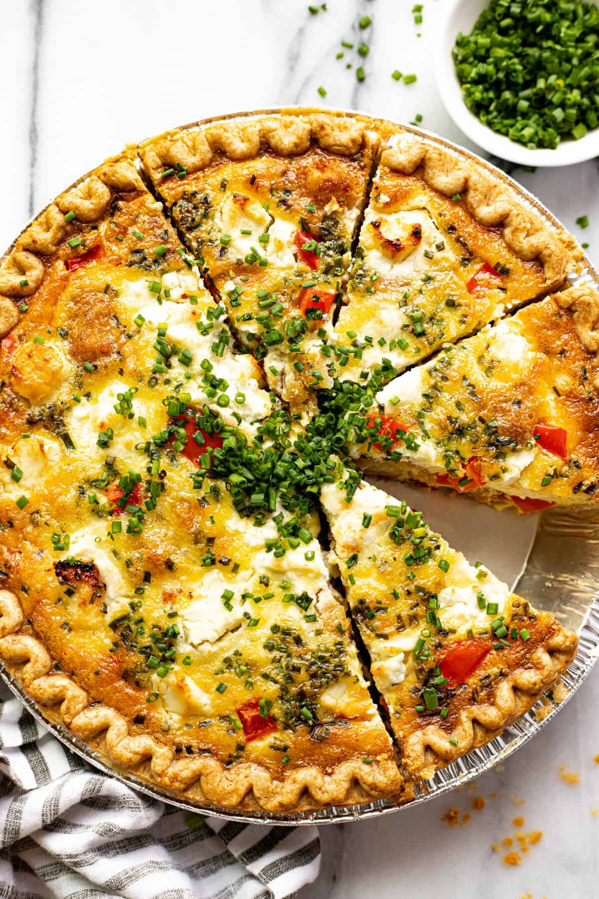 Overhead shot of a sliced quiche with red peppers and potatoes garnished with sliced chives.