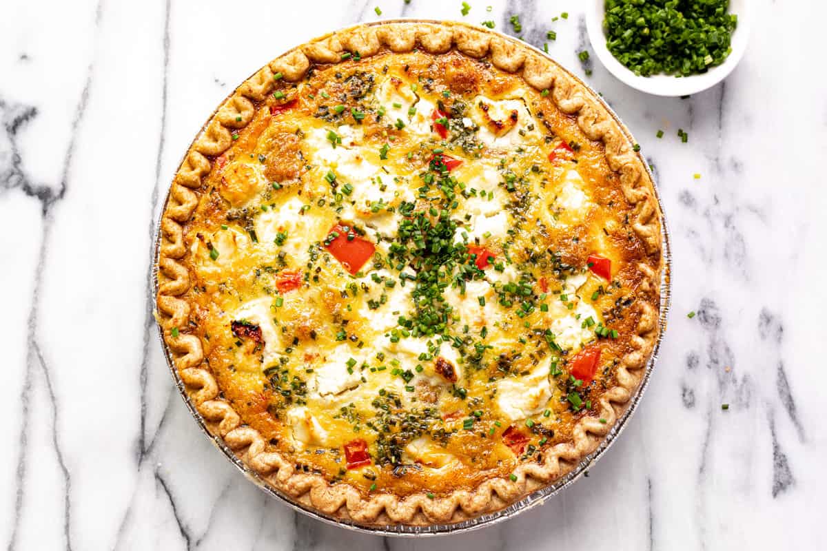 Overhead shot of a quiche with red peppers and potatoes garnished with sliced chives.