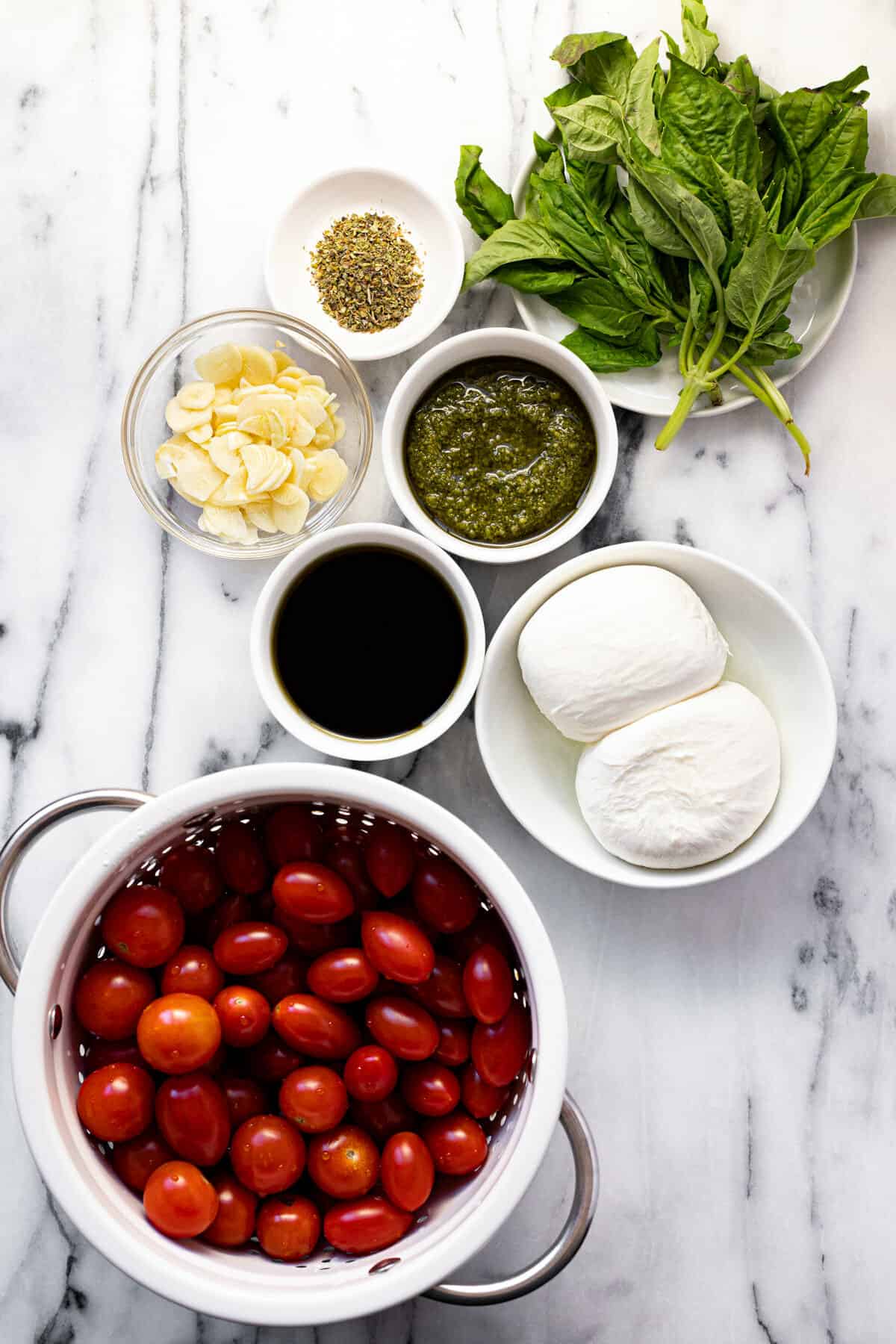 White marble counter top with ingredients to make tomato burrata salad.