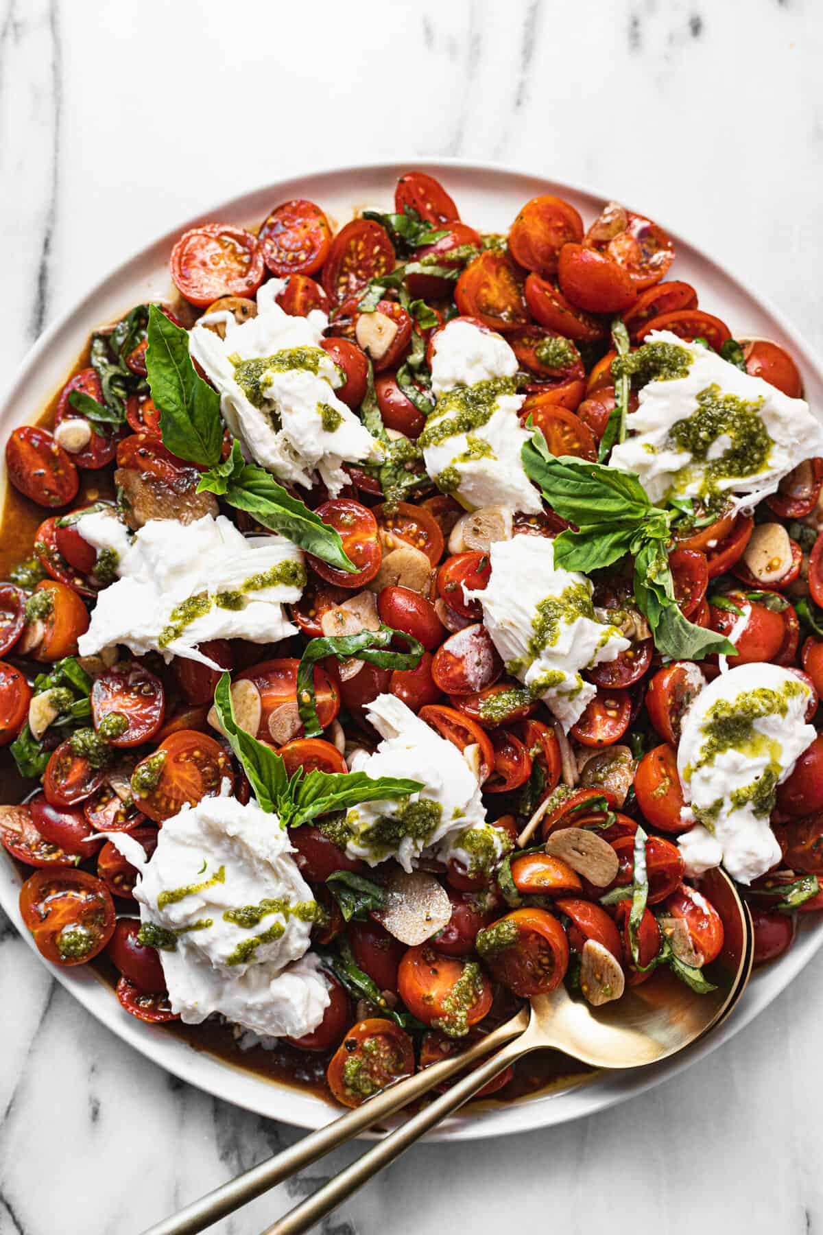 Large white plate with sliced tomatoes and burrata salad garnished with pesto.