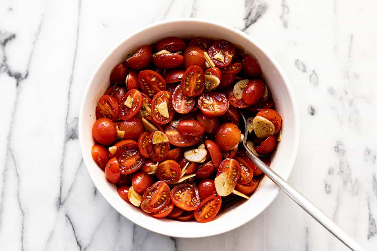 Marinated tomatoes and garlic in a white bowl.