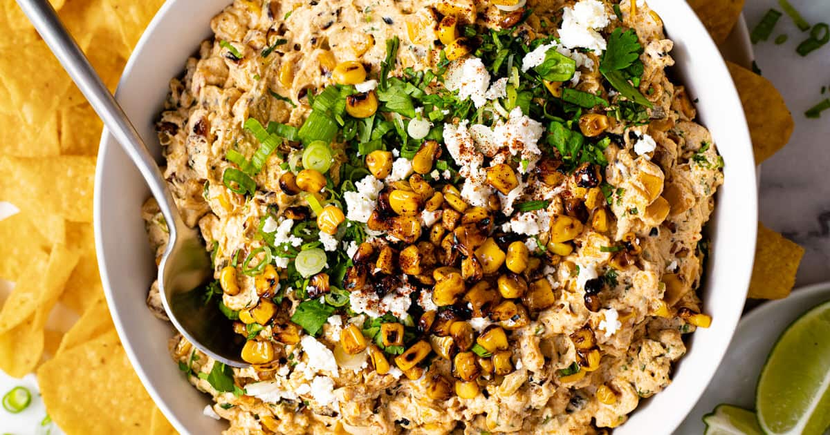 A white bowl of creamy street corn dip topped with Cotija cheese, green onions, and cilantro. 