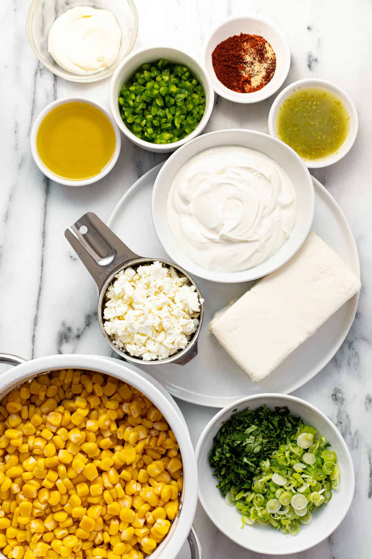 White marble counter top with bowls of ingredients to make creamy corn dip.