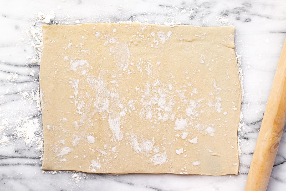 A rectangle of puff pastry dough rolled out onto a marble countertop.
