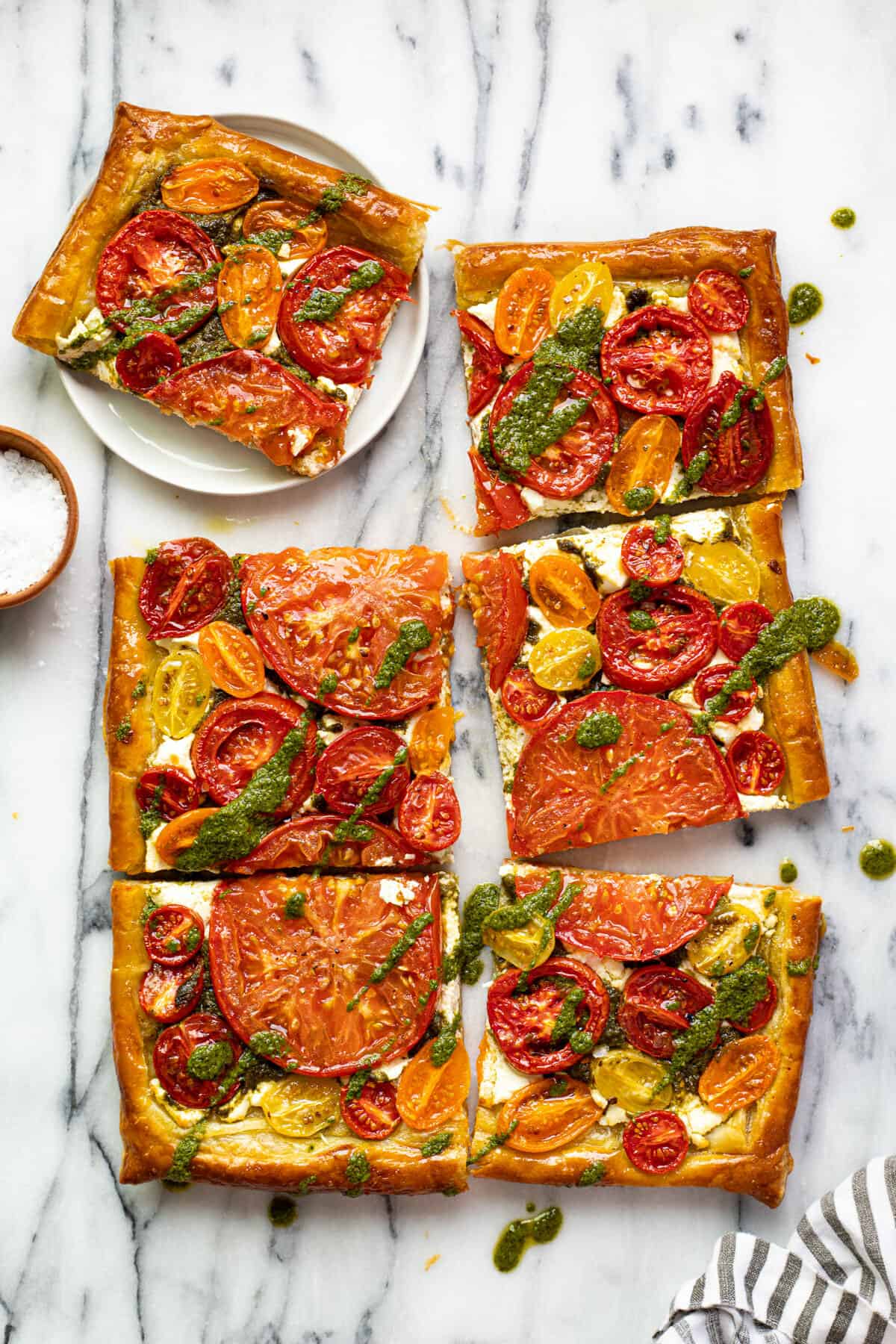 A rectangular puff pastry tomato tart sliced into 6 pieces with 1 piece on a plate.