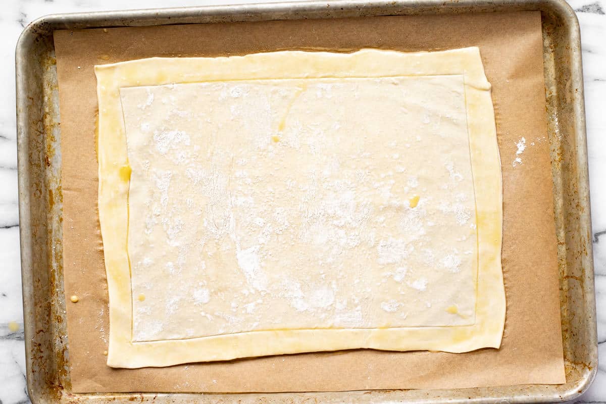 A rectangle of puff pastry dough on a parchment lined baking sheet. 