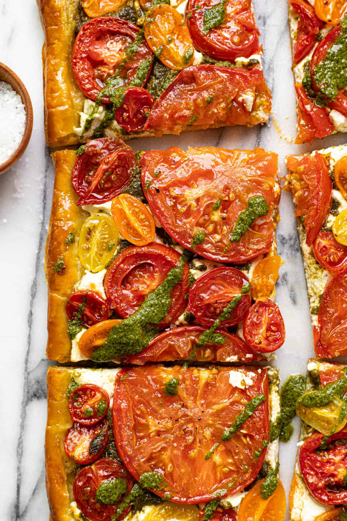Close up of a slice of homemade puff pastry tomato tart drizzled with pesto.