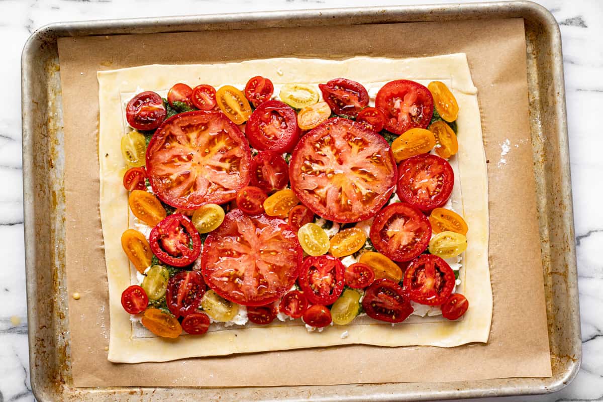 A puff pastry tomato tart on a parchment lined baking sheet ready for the oven.