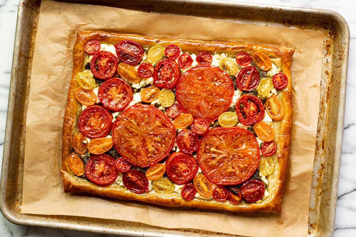 Freshly baked tomato tart on a parchment lined baking sheet.