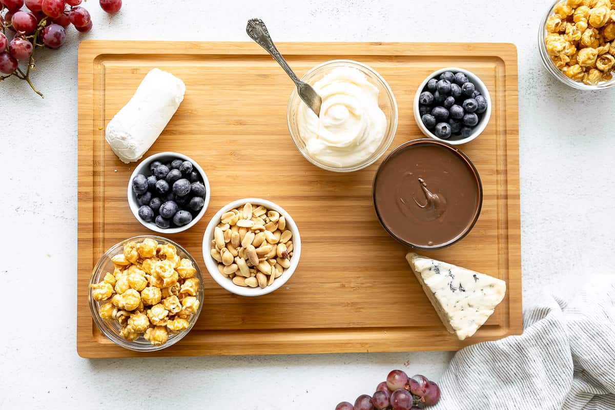 Dips, berries, cheese, and caramel corn on a large dessert charcuterie board.