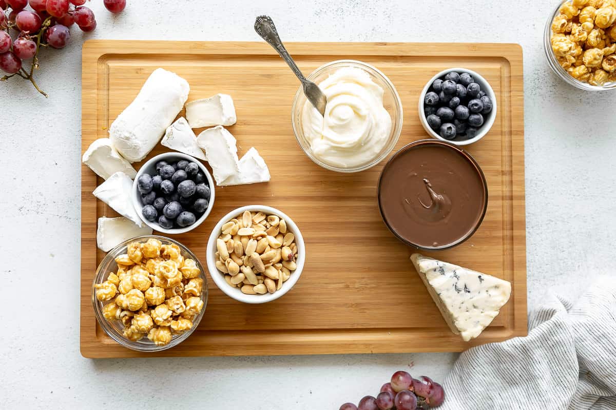 Cheese, nuts, dips, and fruit on a cutting board to make a dessert charcuterie board.