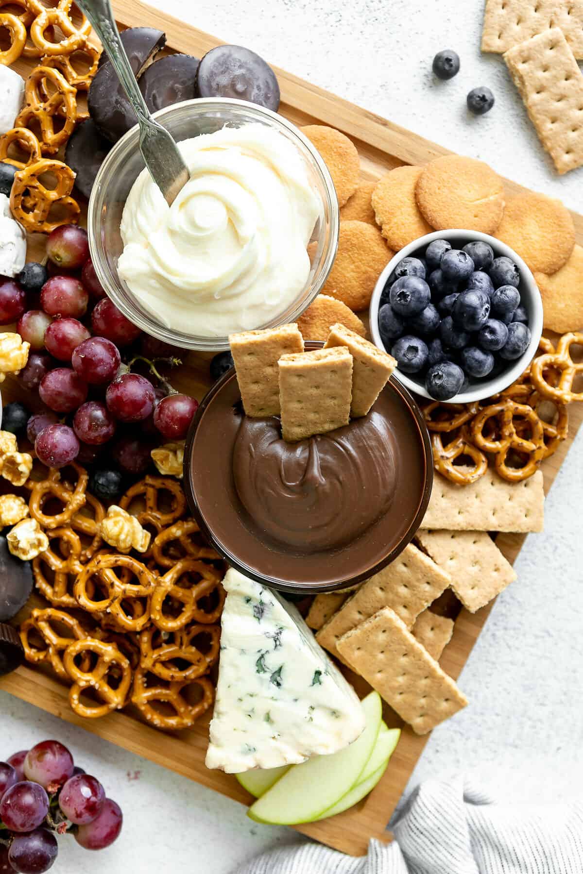 Large dessert charcuterie board filled with fruit, nuts, dips, and candy.